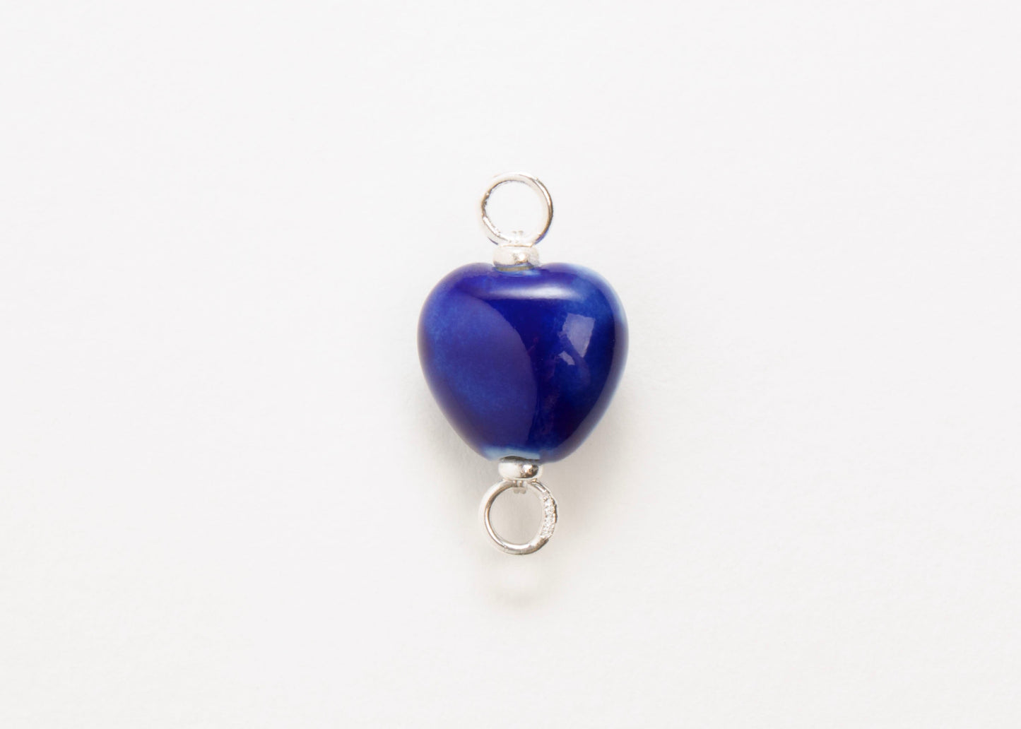 Front close up of a blue glazed porcelain heart-shaped charm with sterling silver looped endings on a white background.
