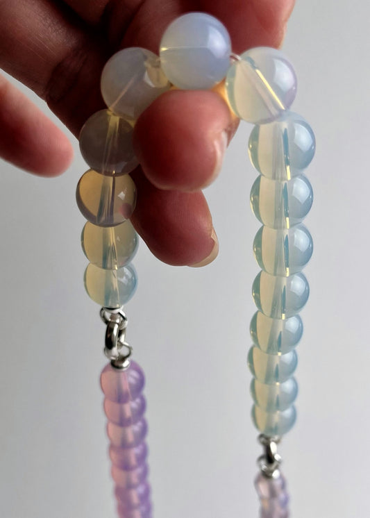 Hand holding a string of Opalite beaded necklace against a plain background