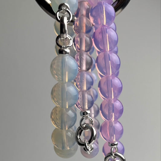 Opalite closed beaded chainlets in 3 colours hanging from a metal hook on a white background