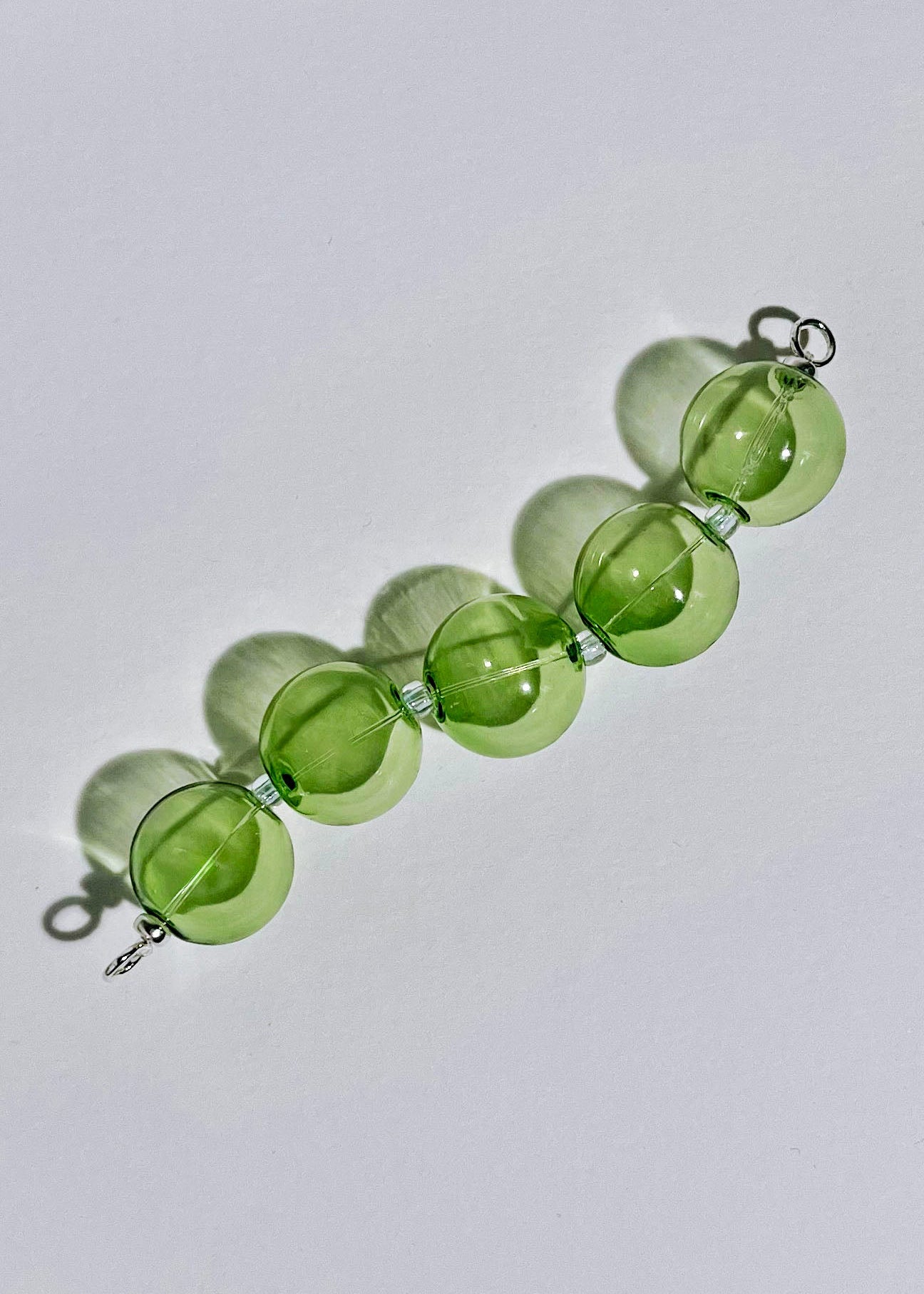 Overhead view of a green chunky bead drop with Sterling Silver endings in a light grey background
