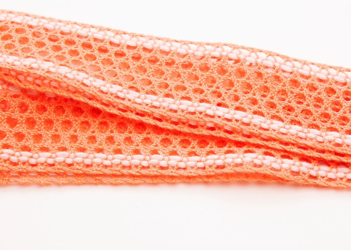 Close up of fabric detail of a cotton fishnet ribbon in orange and white on a white background