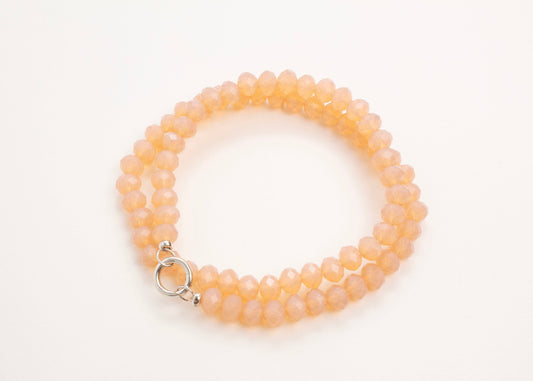 Plan view of a peach glass_bead_strand_wrapped_in_two_loops_on a white background.