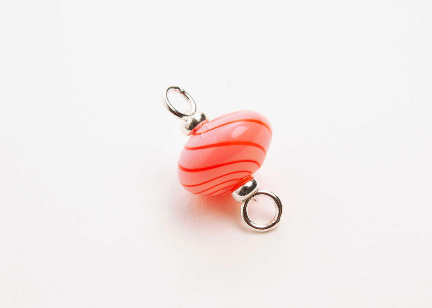 Close up front view of a pink blown glass bead charm with red swirls and Sterling Silver looped endings on a white background.