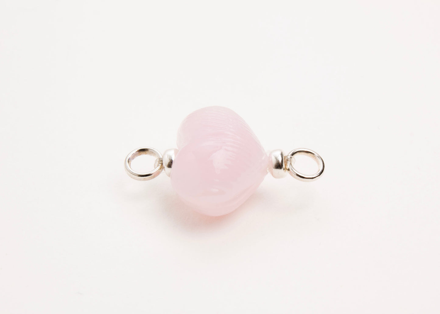 Horizontal close up of pink glass heart charm placed on white background.