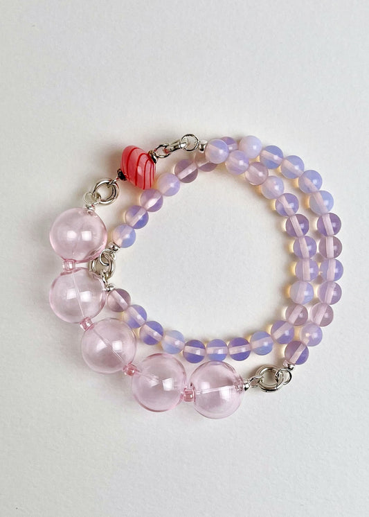 Overhead view of a ready to wear necklace made with pink Opalite bead chainlets, pink chunky glass bead drop and a candy cane top spinner glass charm with Sterling Silver endings arranged in a double loop on a white background