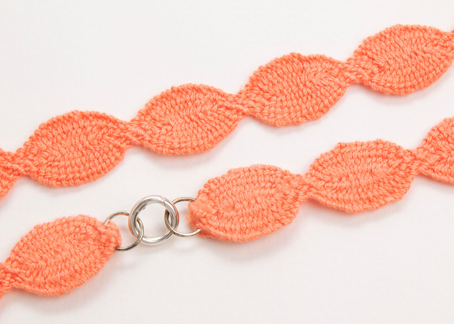 Close up of the Sterling Silver endings of an orange red cotton woven ovals necklace on a white background