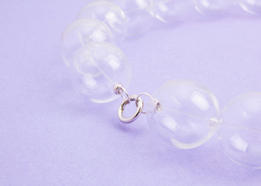 Close up of Sterling Silver looped endings closed of a chunky clear blown glass beads necklace on a lavender background