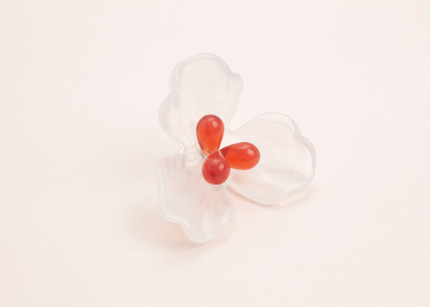 front side view of a clear white resin 3 petal flower charm with glass beads detail on a soft peach background
