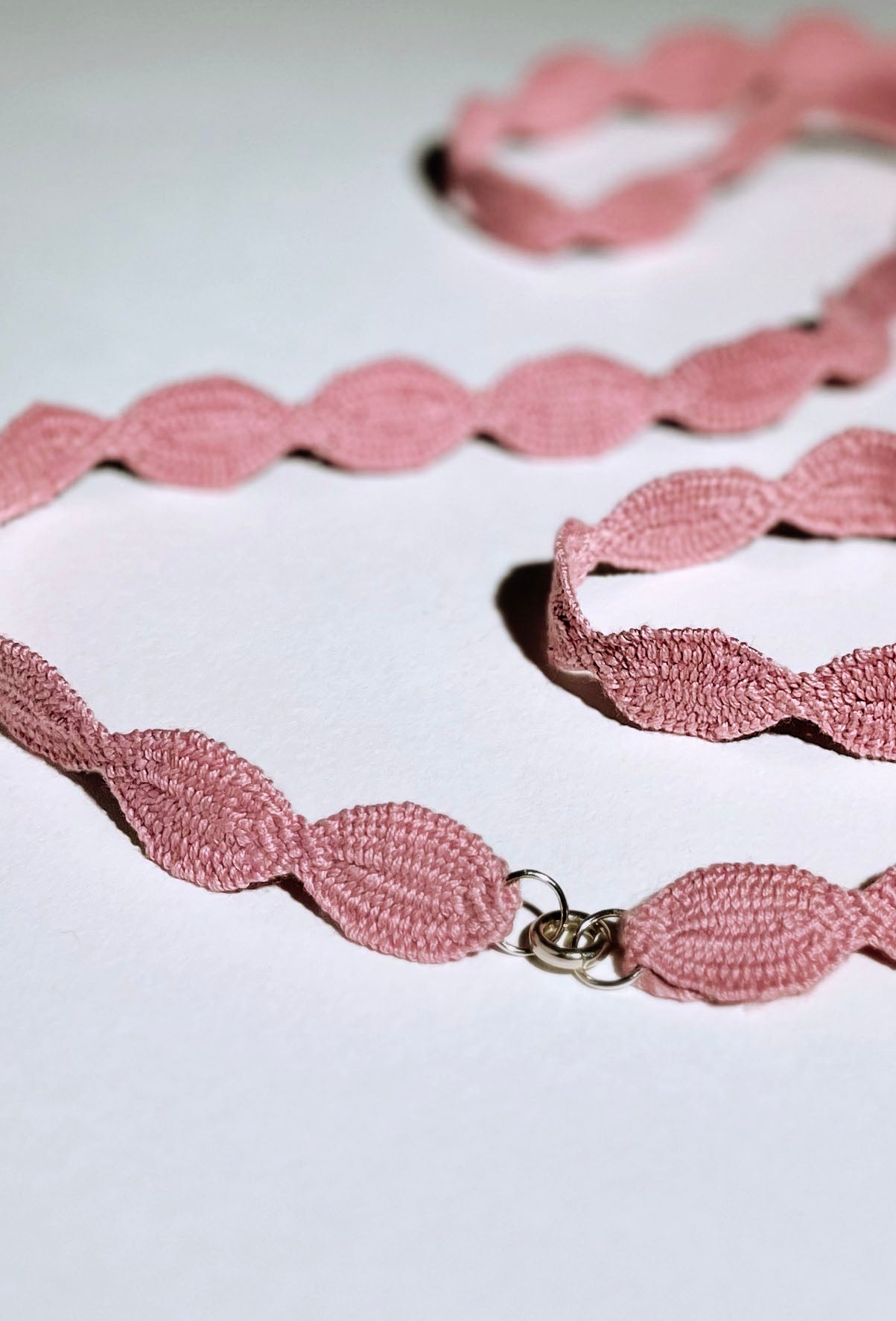 Close view at the fabric and endings detail of a pink cotton interwoven ovals necklace with Sterling Silver endings placed in a double loop on a white background