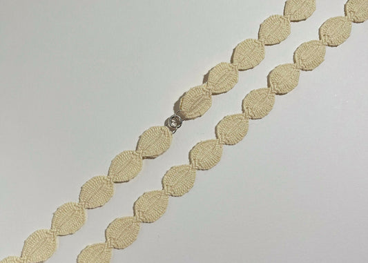 Overhead close look of an ivory cotton woven ovals necklace with Sterling Silver endings placed in diagonally on an ivory background