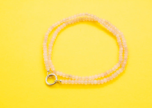 Plan view of a pink quartzite beaded necklace with Sterling Silver looped endings wrapped into two loops on a yellow background