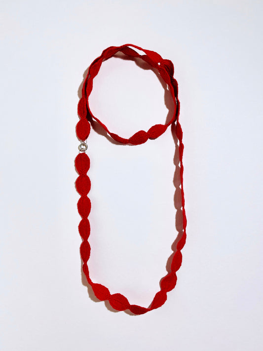 Overhead view of a red interwoven cotton ovals necklace with Sterling Silver endings double looped into a chocker with long drop on a white background
