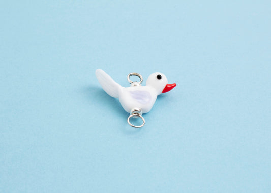 Front view of a white_lamp_work_bird charm_with an orange beak and lavender wings on a sky blue background