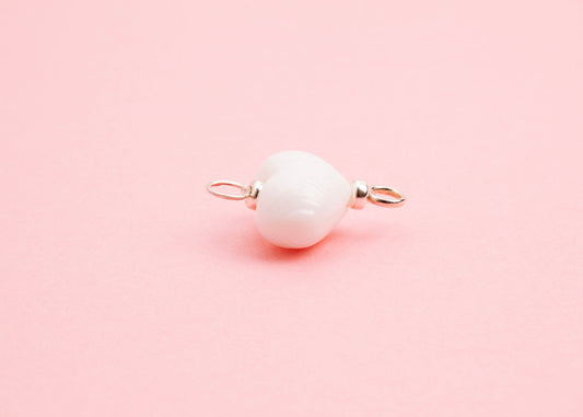 Side view of white lampwork glass heart charm with Sterling Silver looped endings on a pink background