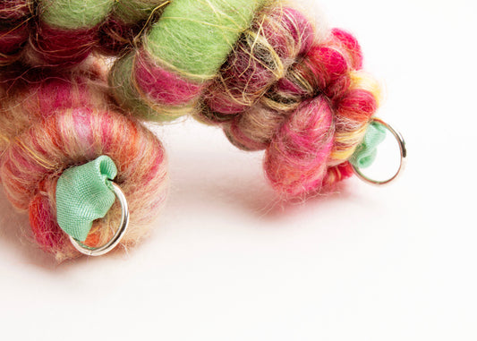 Close up of the Sterling Silver looped endings of a wool yarn closed necklace in persimmon, peach, butter yellow, mint and forest green on a white background