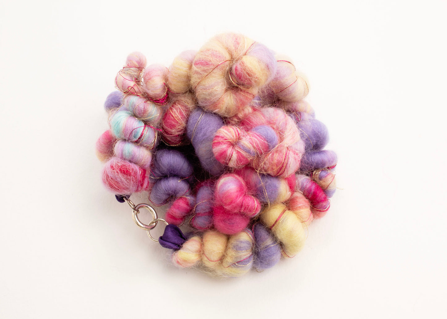Plan view of wool yarn necklace in a knot in cream, lavender, deep pink, purple and gold with Sterling Silver looped endings on a white background