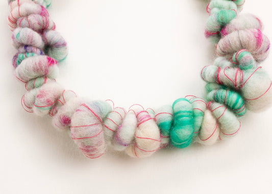 Close up drop detail of a wool yarn necklace in teal, pink and deep pink on a white background