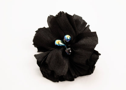 Front view of a black silk flower charm with glass detail in center on a white background.