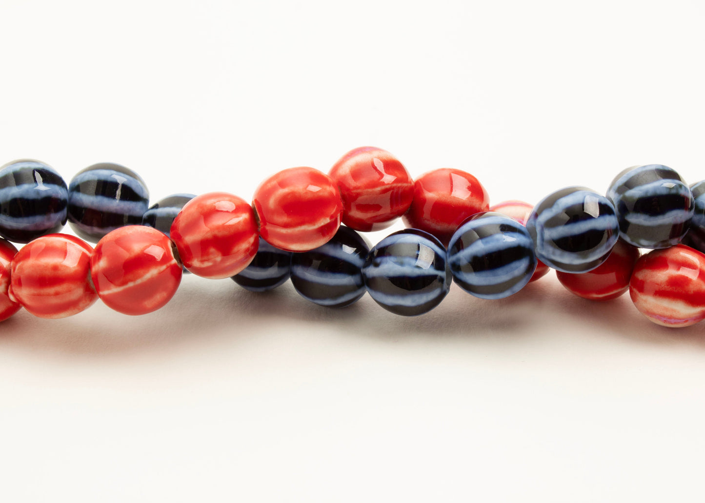Front view of a red and a blue porcelain bead necklaces twisted together on a white background