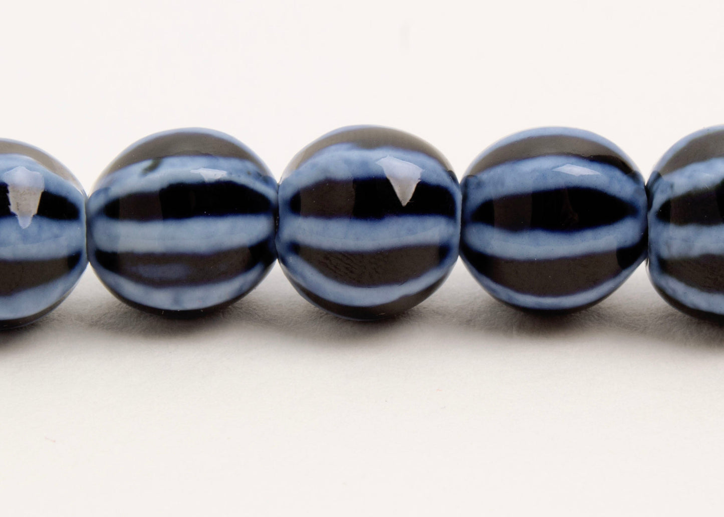 Close up of a dark blue round porcelain bead necklace with bumpy light stripes on a white background