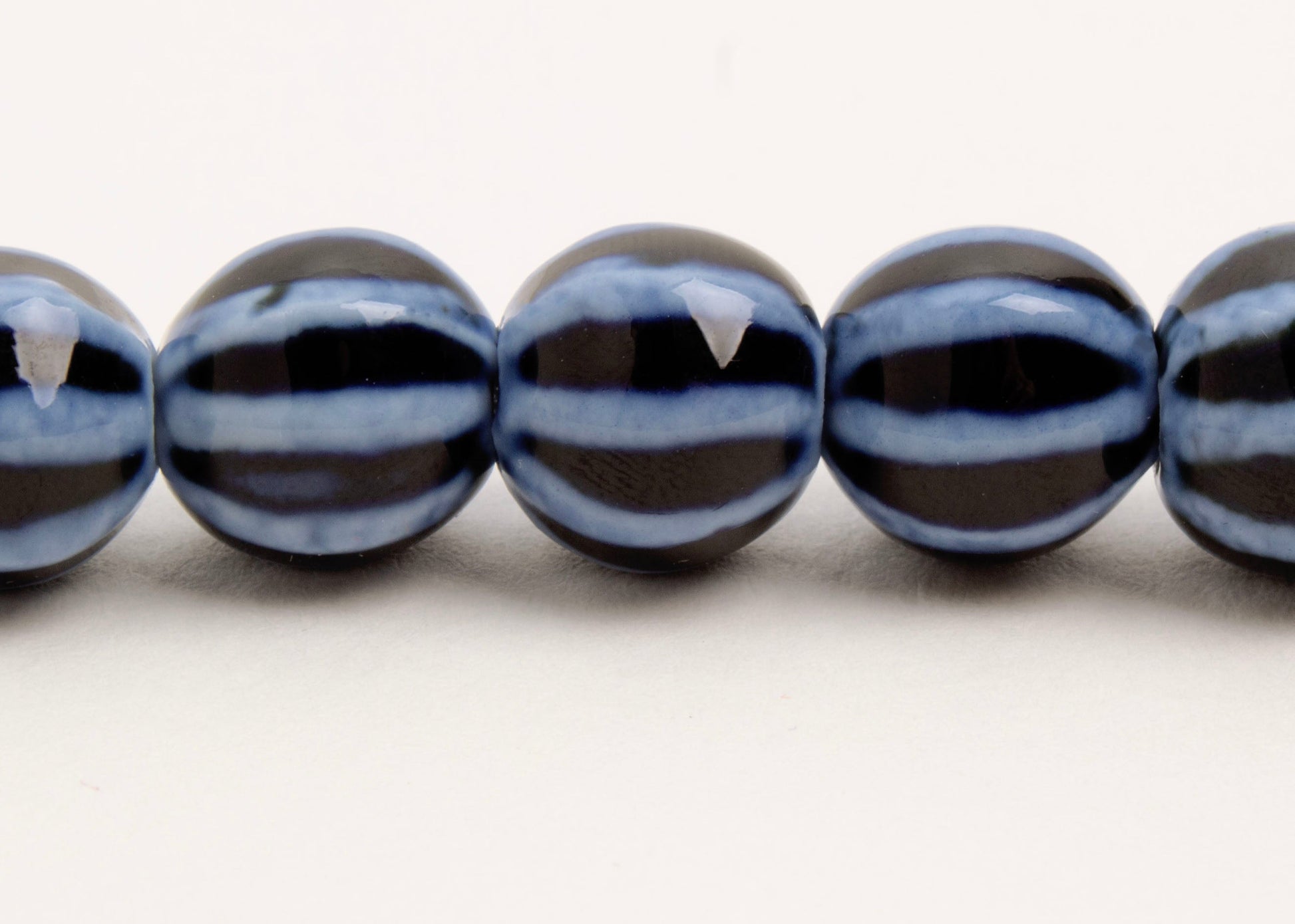 Close up of a dark blue round porcelain bead necklace with bumpy light stripes on a white background