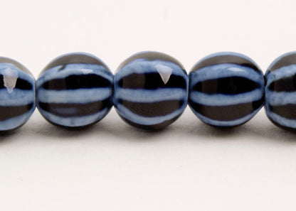 Close up of a dark blue round porcelain bead necklace with bumpy light stripes on a white background