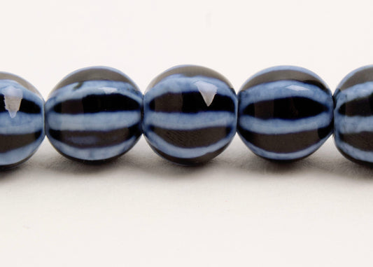 Close up of a dark blue round porcelain bead necklace with bumpy light stripes on a white background
