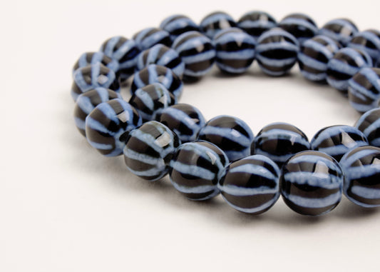 Close up of dark blue round porcelain beads with light blue bumpy stripes wrapped in two loops on a white background