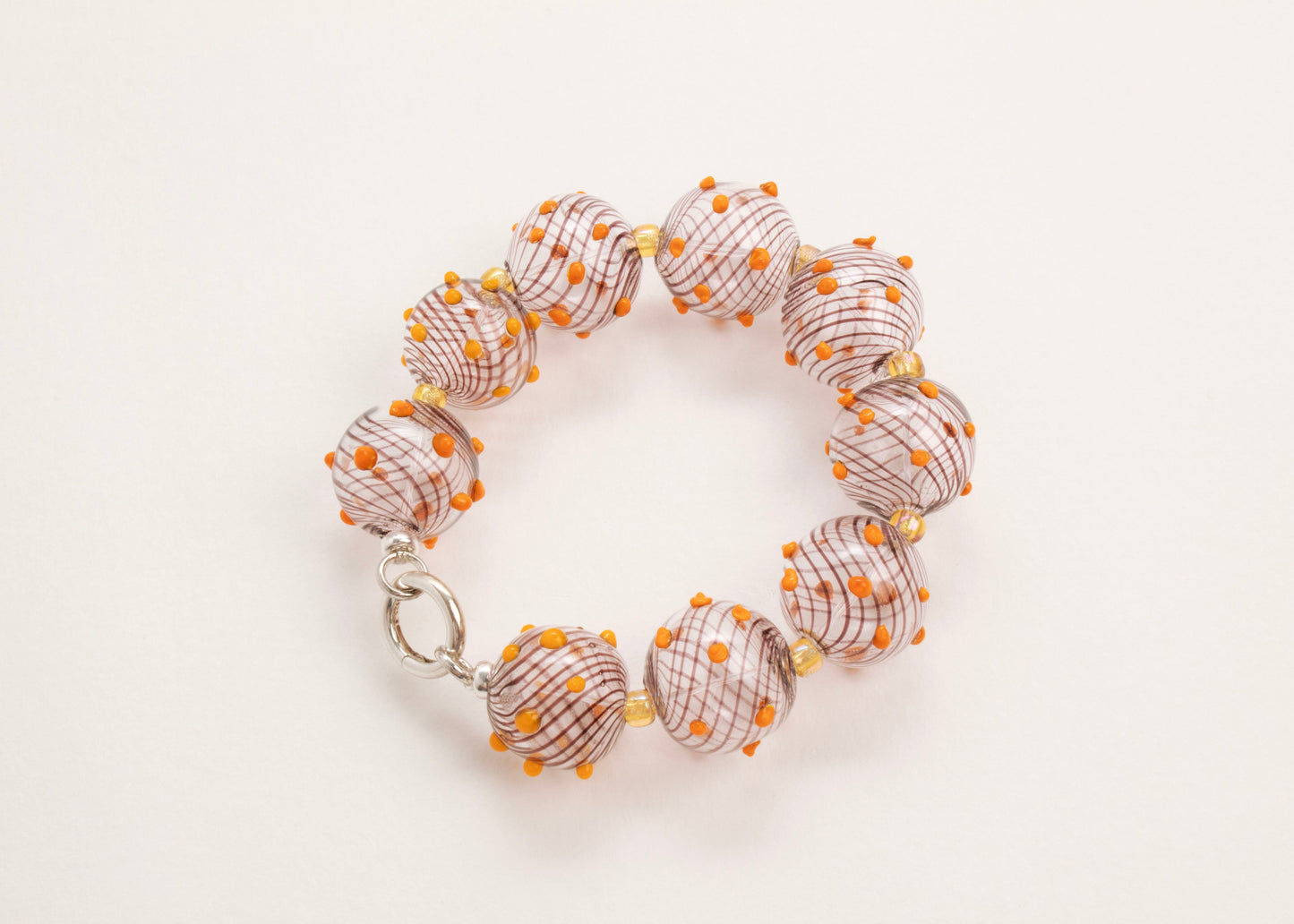 Plan view of a closed clear blown glass bead strand with brown swirls, orange bumps and butter yellow separators on a white background