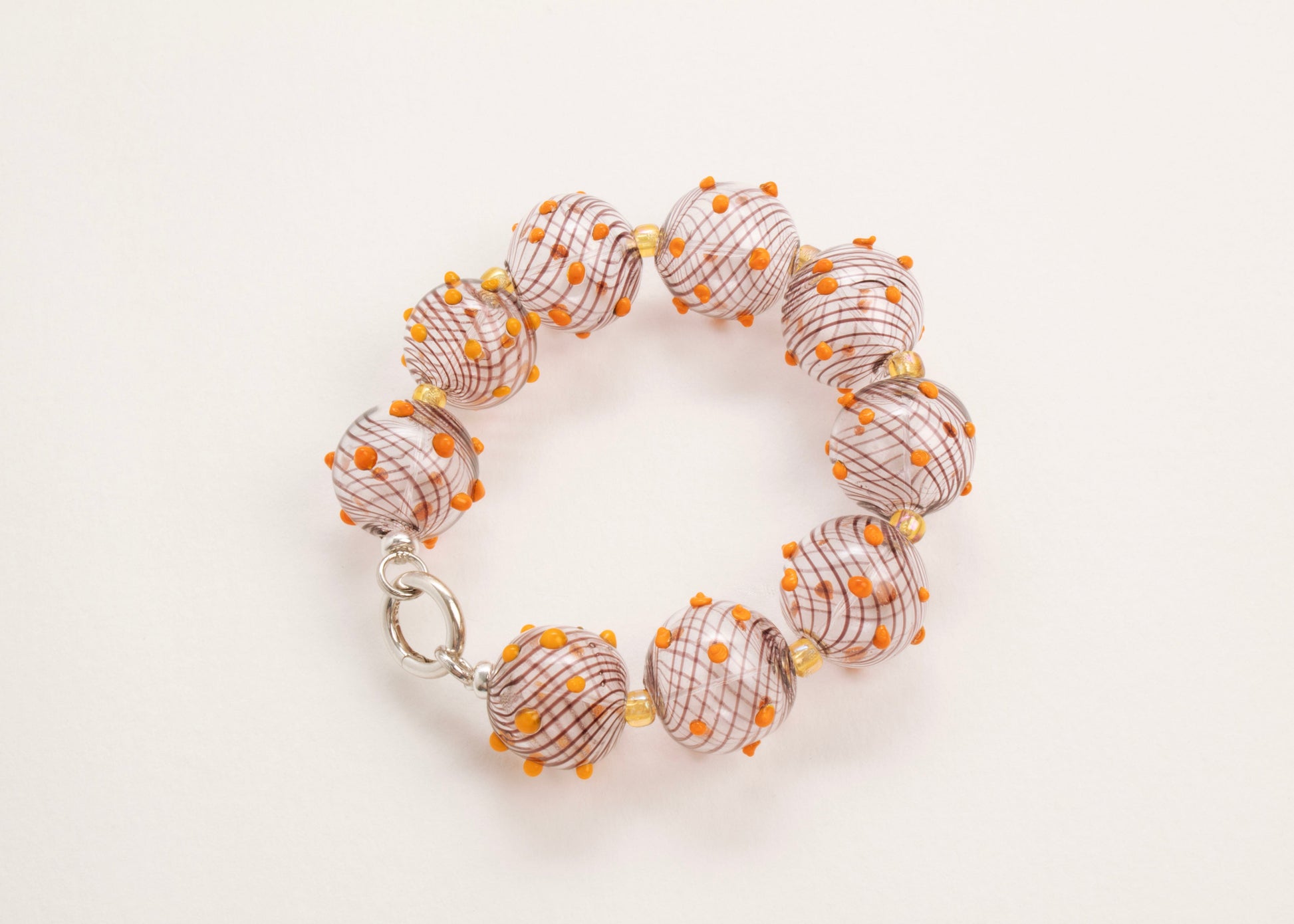 Plan view of a closed clear blown glass bead strand with brown swirls, orange bumps and butter yellow separators on a white background