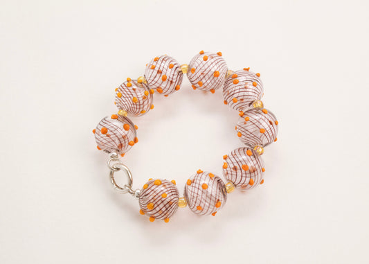 Plan view of a closed clear blown glass bead strand with brown swirls, orange bumps and butter yellow separators on a white background