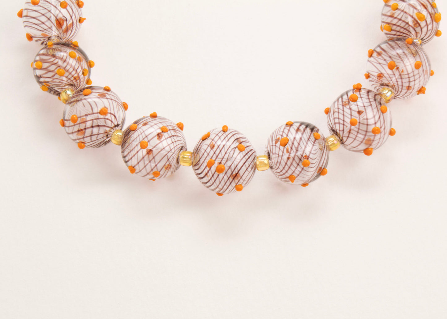 Close up of the drop detail of a clear blown glass bead strand with brown swirls orange bumps and butter yellow separators on a white background