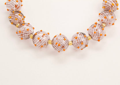 Close up of the drop detail of a clear blown glass bead strand with brown swirls orange bumps and butter yellow separators on a white background