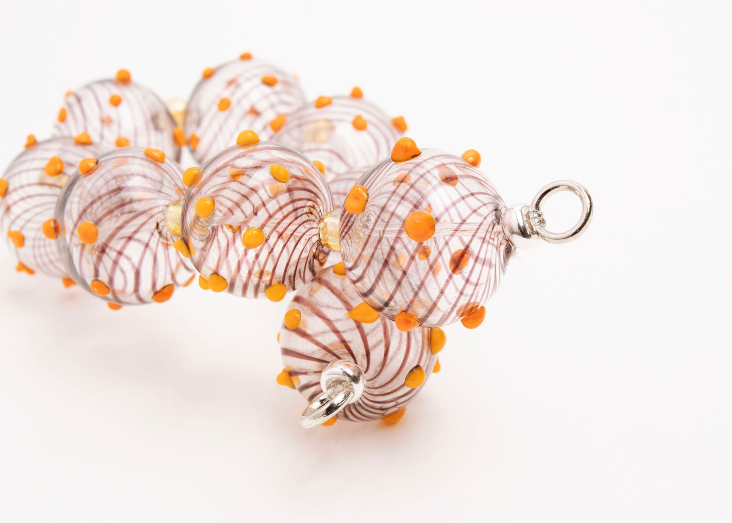 Close up of the sterling silver lopped endings of a clear blown glass bead strand with brown swirls, orange bumps and butter yellow separators on a white background