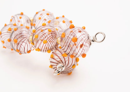 Close up of the sterling silver lopped endings of a clear blown glass bead strand with brown swirls, orange bumps and butter yellow separators on a white background
