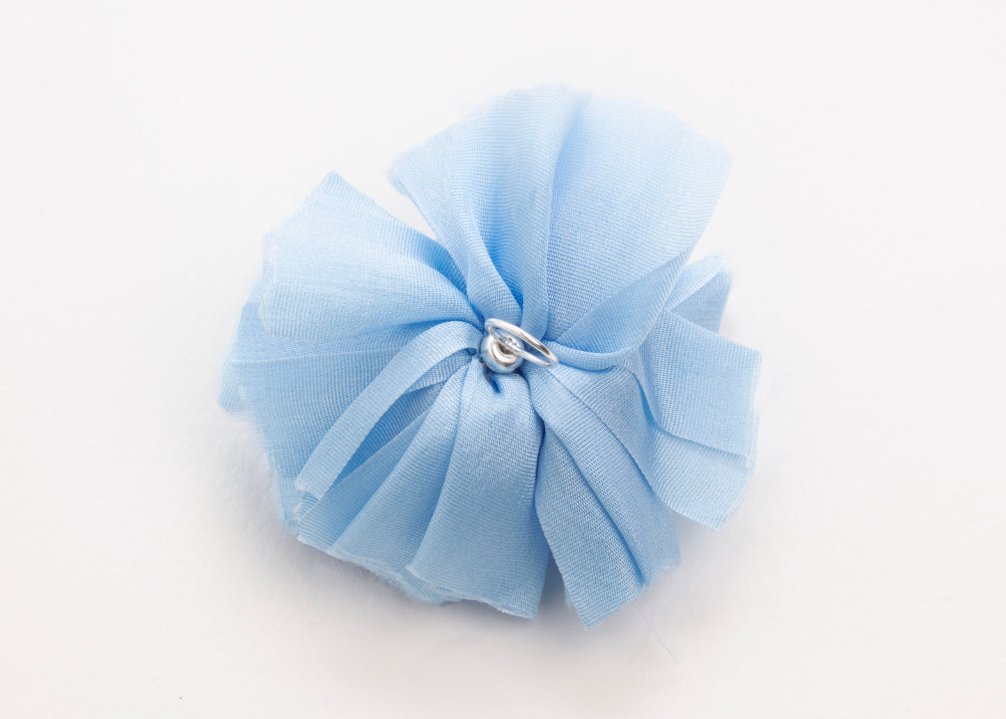 Back view of a cerulean silk flower charm with sterling silver loop ending on a white background.