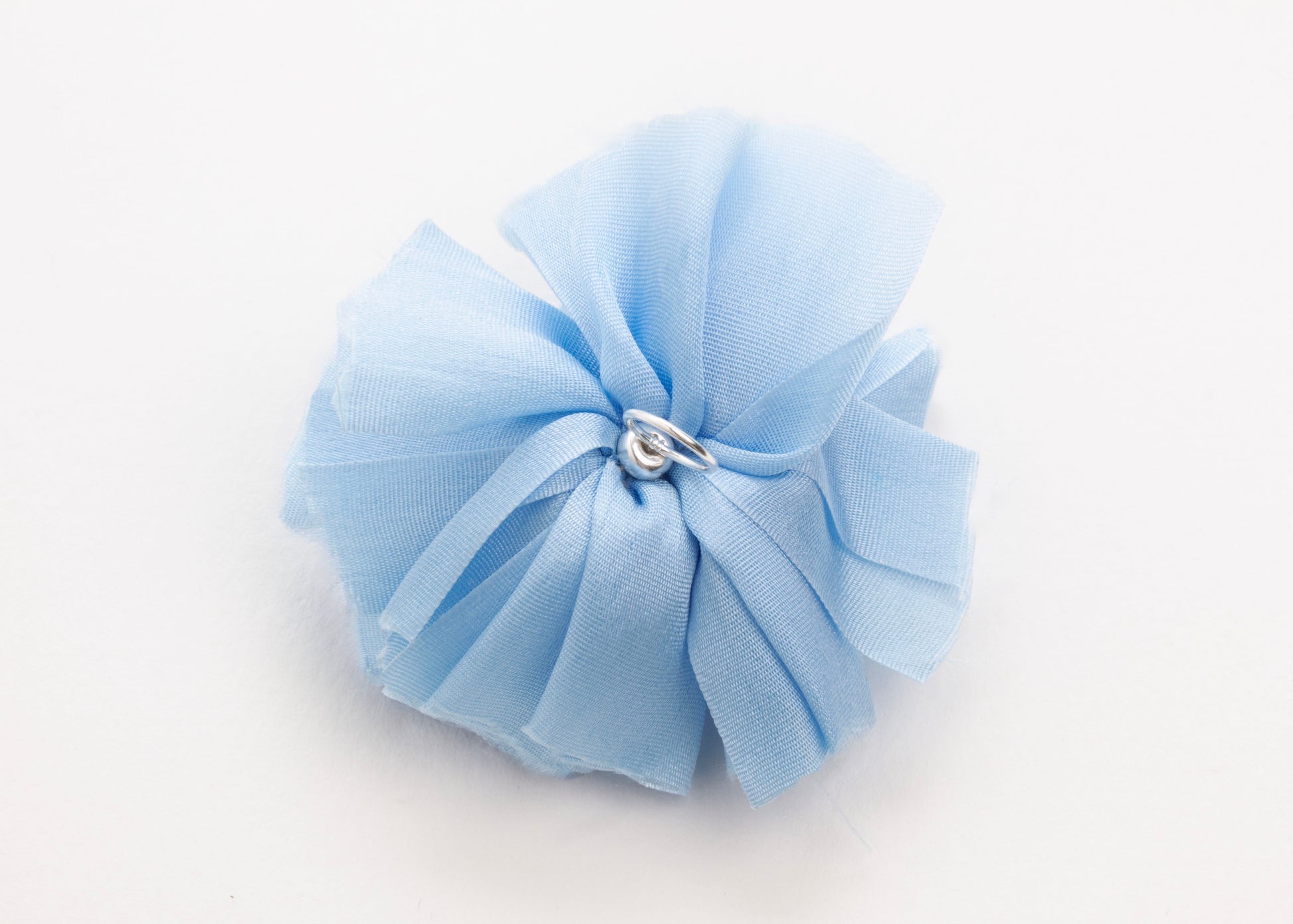 Back view of a cerulean silk flower charm with sterling silver loop ending on a white background.