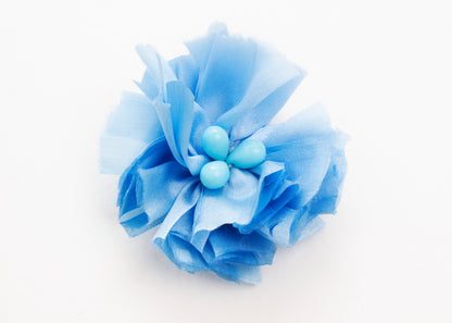 Front view of a cerulean silk flower charm with glass detail in center on a white background.