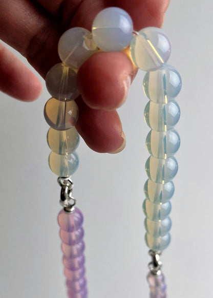 Hand holding a string of Opalite beaded necklace against a plain background