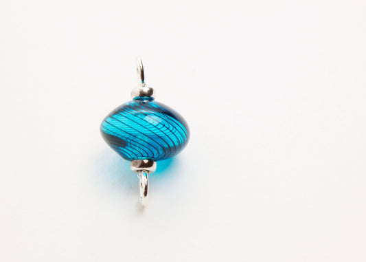 Glassblown blue charm and connector with dark blue swirls in the shape of a spinner with sterling silver endings, on a white background. Straight centre front view. 