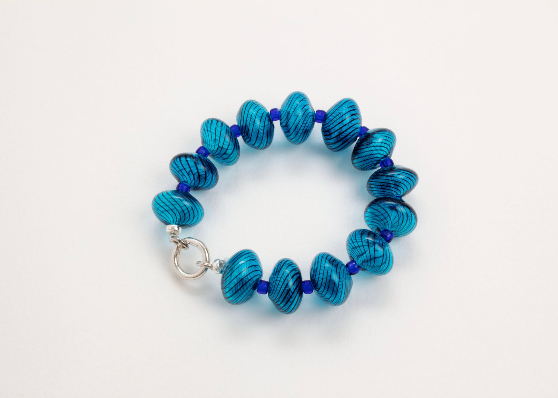 Close up of a closed cyan blown glass bead strand with dark blue swirls and electric blue separators on white background
