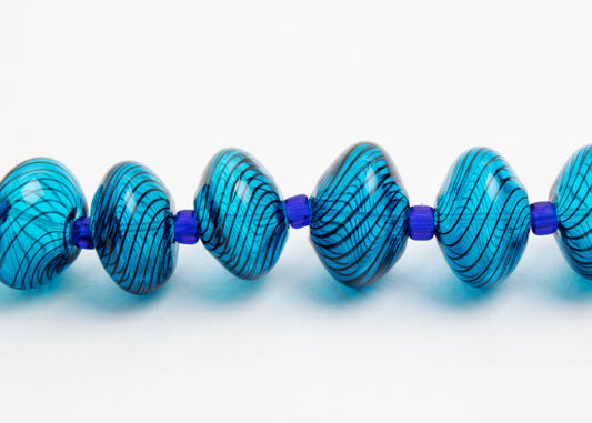 Close up front horizontal view of a cyan blue blown glass bead strand with dark blue swirls and electric blue separators on white background