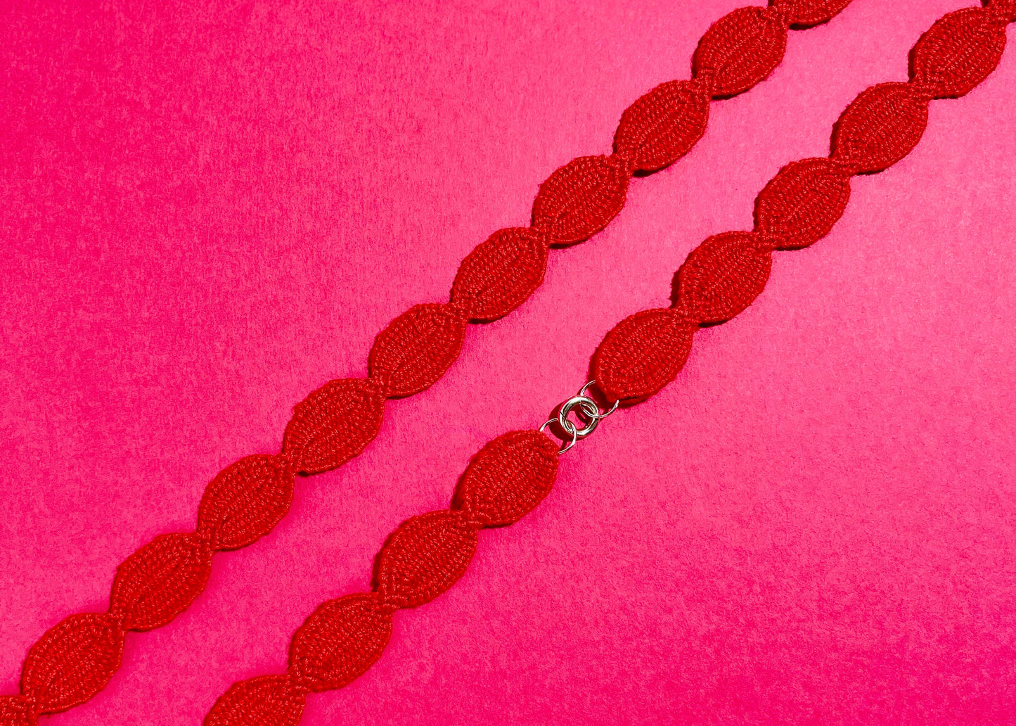 Overhead close look at the fabric and endings of a red interwoven cotton ovals necklace with Sterling Silver endings placed diagonally on a deep pink background