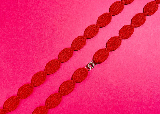 Overhead close look at the fabric and endings of a red interwoven cotton ovals necklace with Sterling Silver endings placed diagonally on a deep pink background
