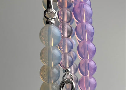 Opalite closed beaded chainlets in 3 colours hanging from a metal hook on a white background