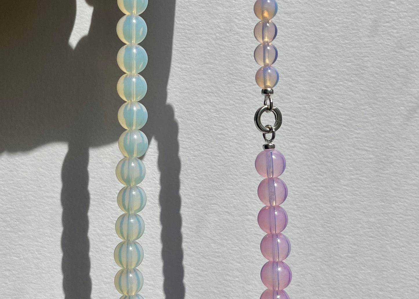 Front view in the sun light of an Opalite beaded necklace made of three chainlets in three different colours agains a white wall