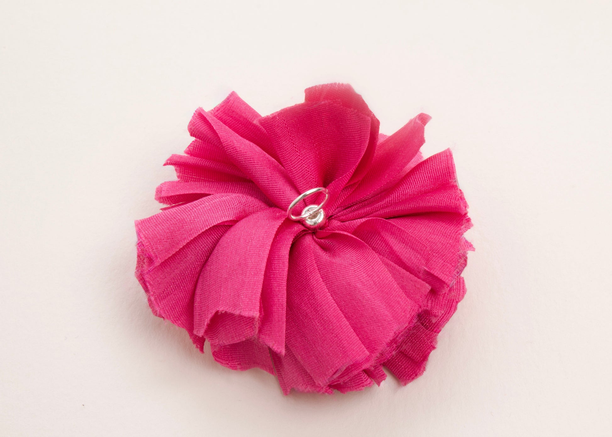 Back view of a fuchsia silk flower charm with sterling silver loop ending on a white background.
