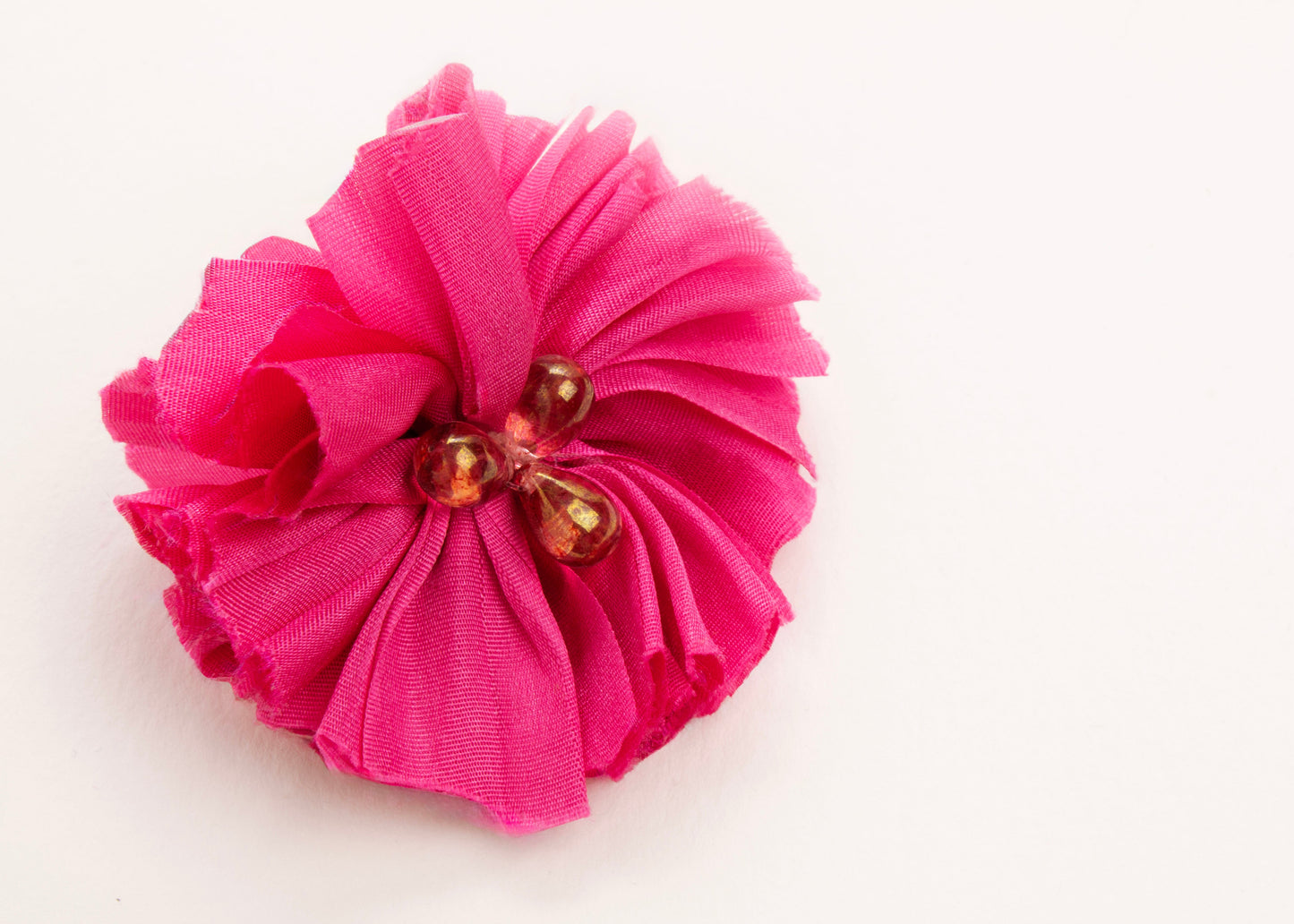 Front view of a fuchsia silk flower charm with glass detail in center on a white background.