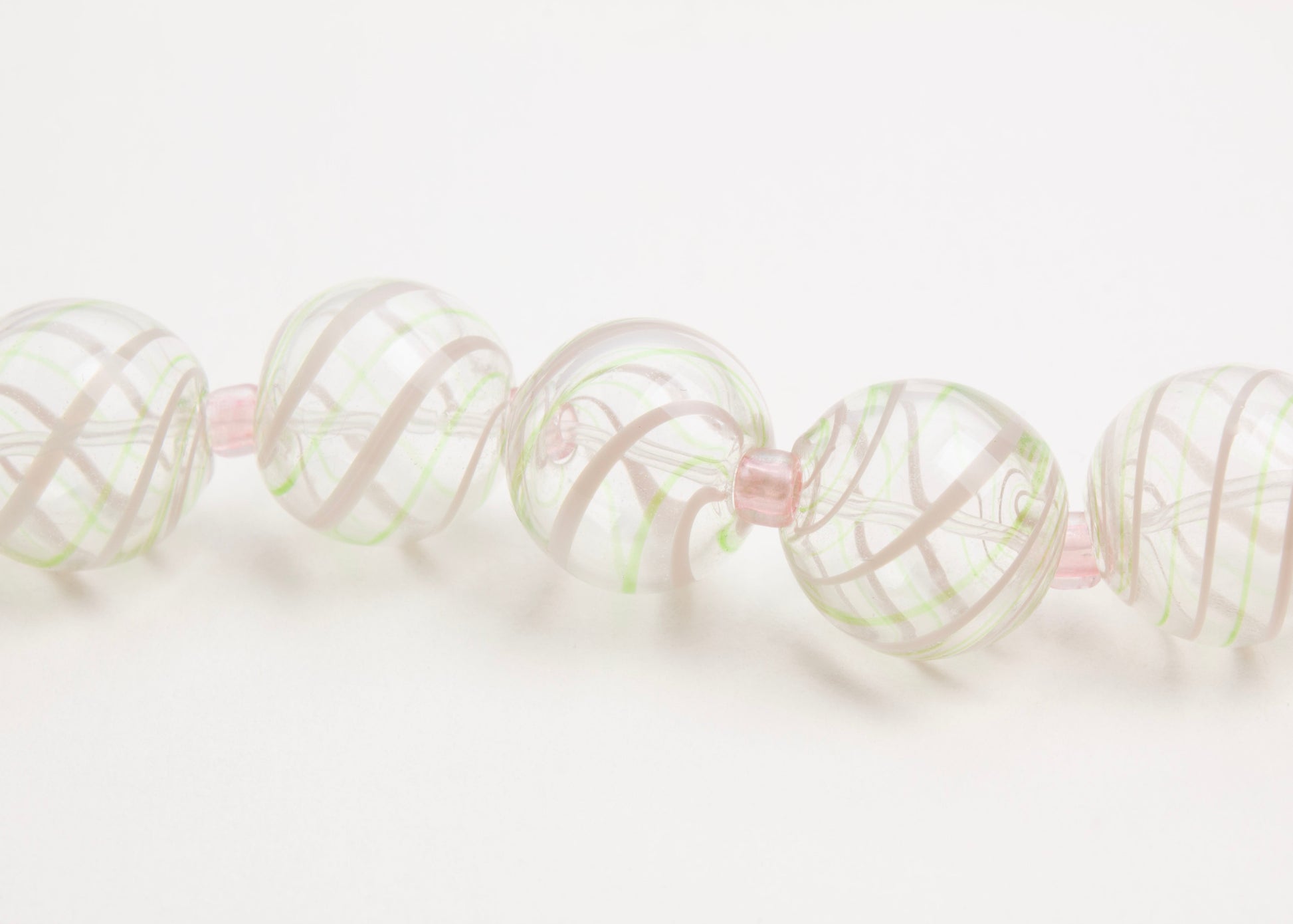 Close up front view of a clear blown glass bead strand with green and pink swirls and pink glass separators horizontal on white background