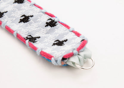 Close up of Sterling Silver looped ending of a reversible cotton woven strap bracelet in houndstooth pattern in grey blue with embroidered borders in fuchsia and light blue on a white background.